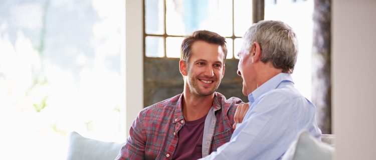 Senior Father With Adult Son Relaxing On Sofa At Home